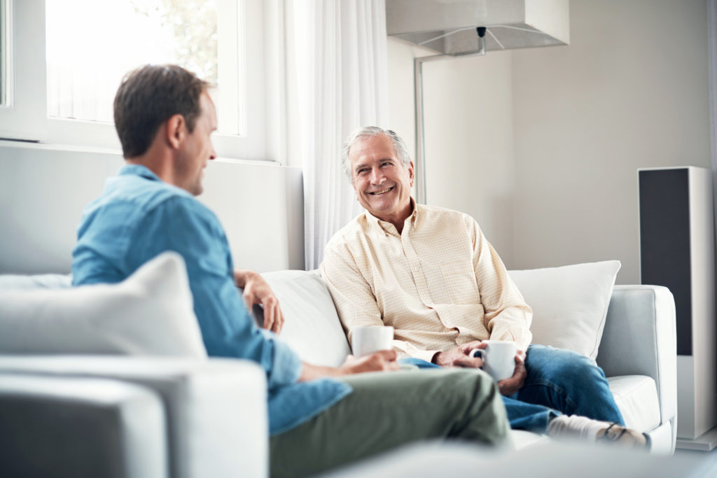 Shot of a young man and his elderly father having a chat over coffee on the sofa at home