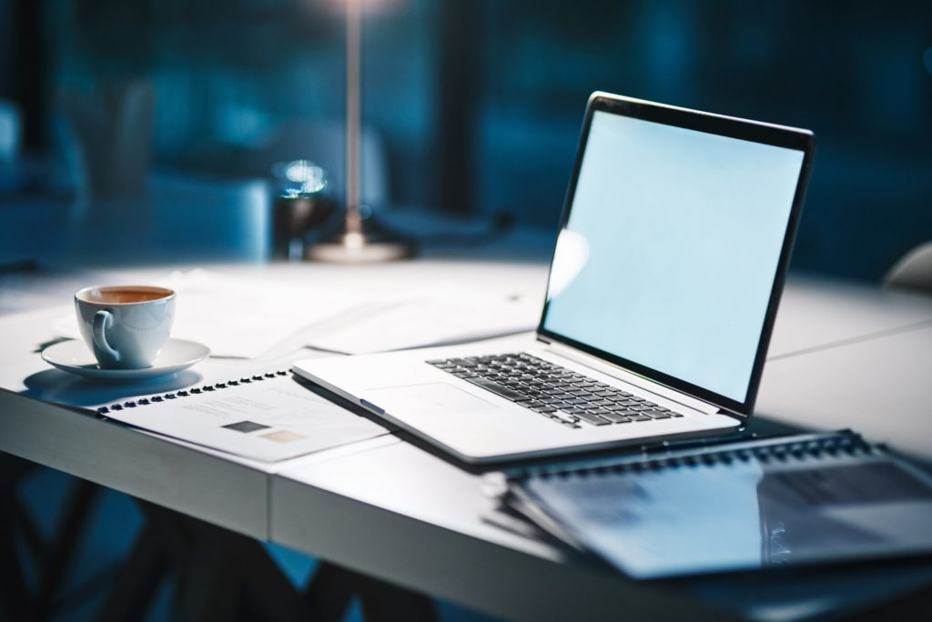 Laptop open on a desk on top of papers and next to a coffee