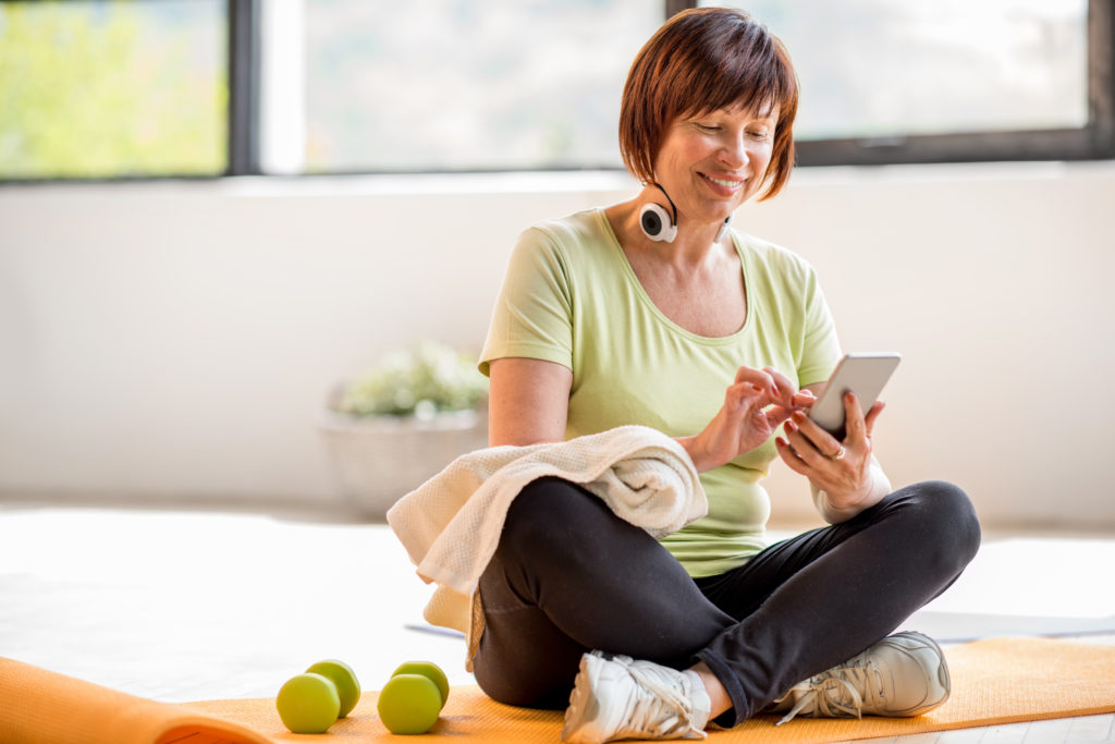 Older woman working out with weights, headphones, and checking her smartphone