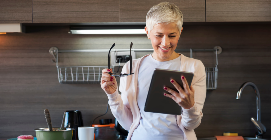 Mature woman using digital tablet at kitchen, looking for recipe on internet