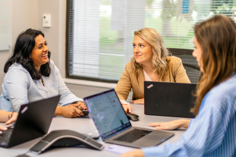 Three women sit at table with laptops