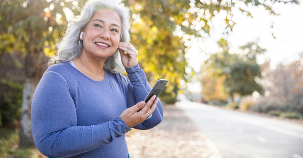 Woman holding phone on road with foliage