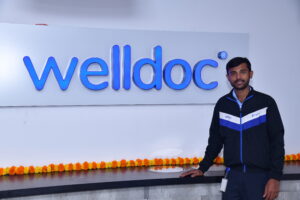 An employee standing in front of the Welldoc sign at the Bangalore Center for Innovation, Research and Development (CIDR) office location.