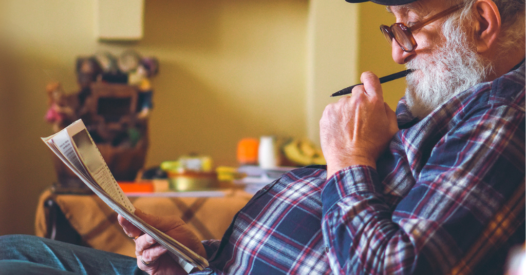 Man leaning against a wall reading a paper with a pencil in his mouth